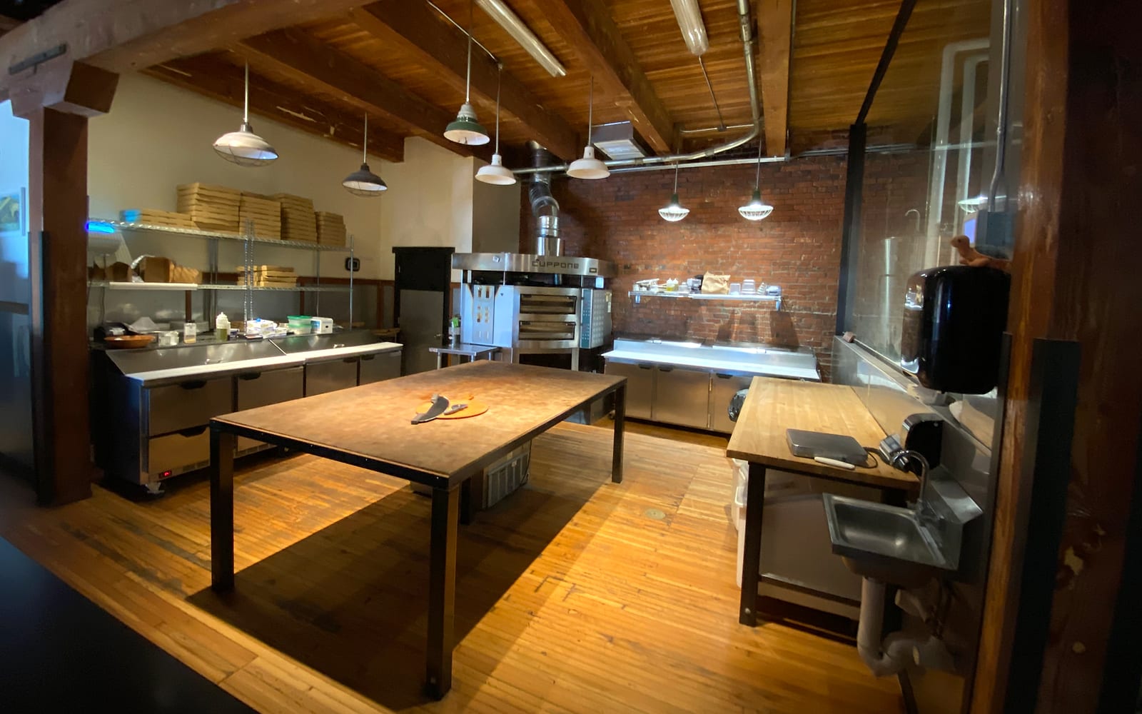 The Wheel's kitchen: a butcher block table in warm light, the brick floor oven against an old brick wall under timber beams