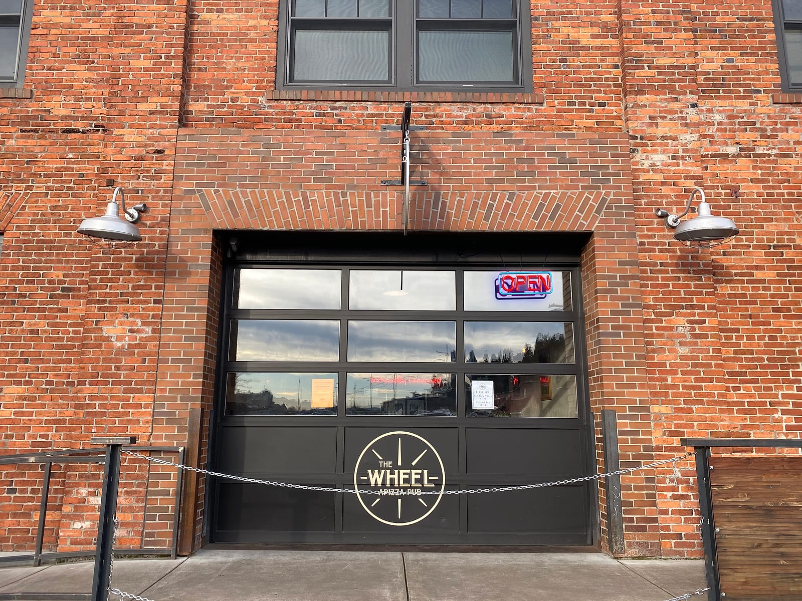 The brick building entrance with a glass garage door bearing the Wheel sign and an open sign
