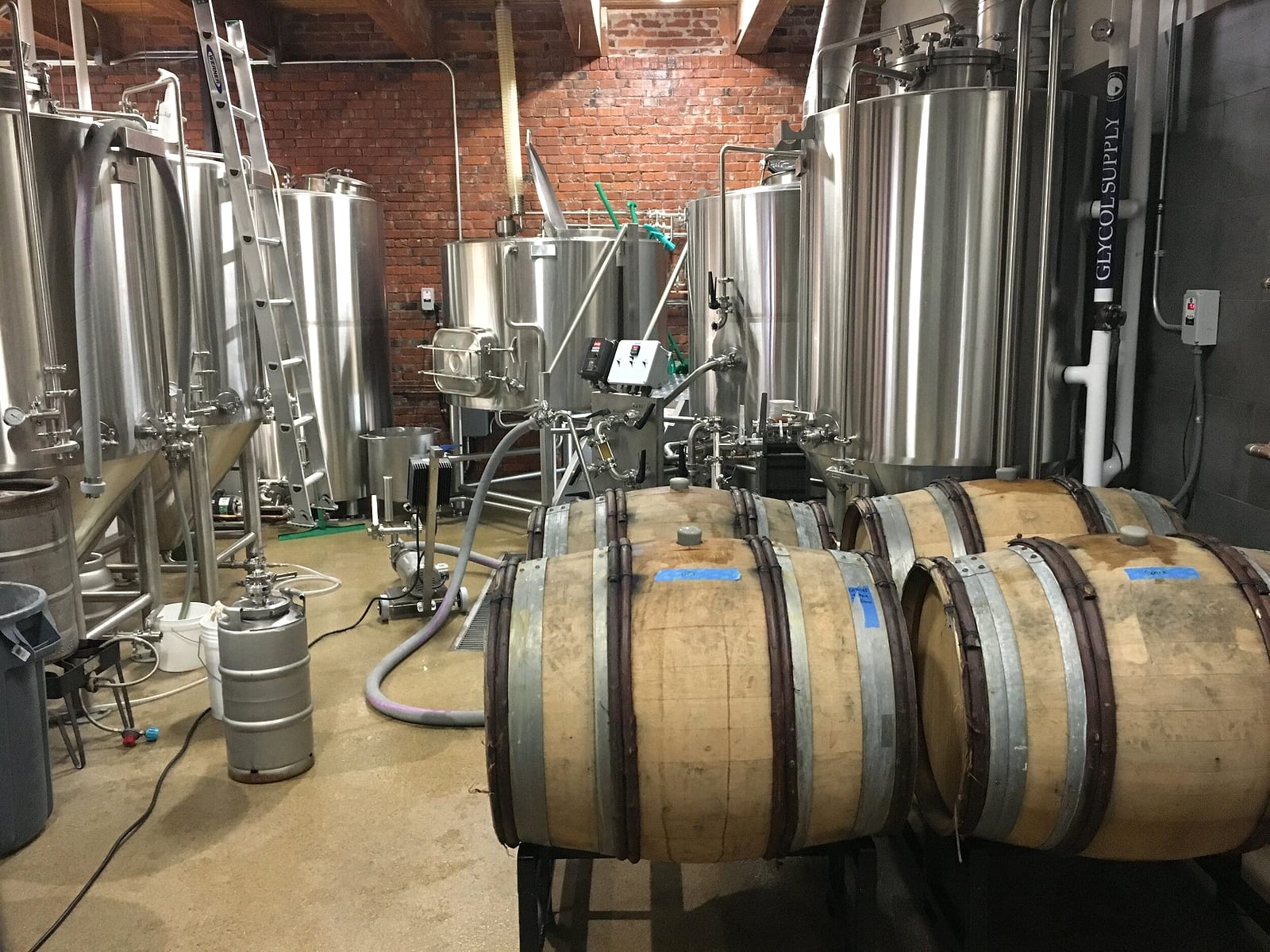 The brewhouse: stainless fermentation tanks and wooden barrels against a brick wall